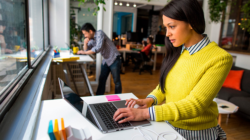 Woman in a yellow sweater working on a laptop.